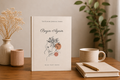 Book titled 'Begin Again' from The Bloom Journal Series on a wooden table with a cup and pen.