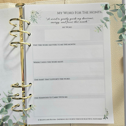 February Eucalyptus Monthly Planner printable A5 PDF preview.
A close-up of a gold-ring binder planner insert page titled 'MY WORD FOR THE MONTH' with writing prompts, shown on a beige textured background with eucalyptus leaves around it.