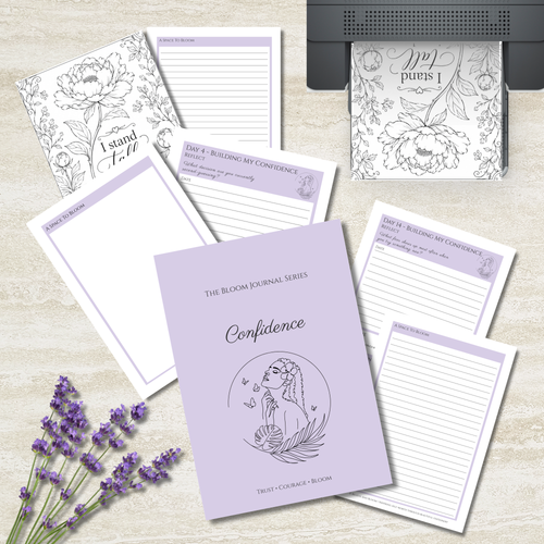 A flat-lay of a journaling and affirmation kit featuring a lavender hardcover journal titled 'Confidence' and several matching lined notepads and printable pages with floral line art and lavender accents, arranged on a light wood surface with lavender sprigs and a printer visible in the background.