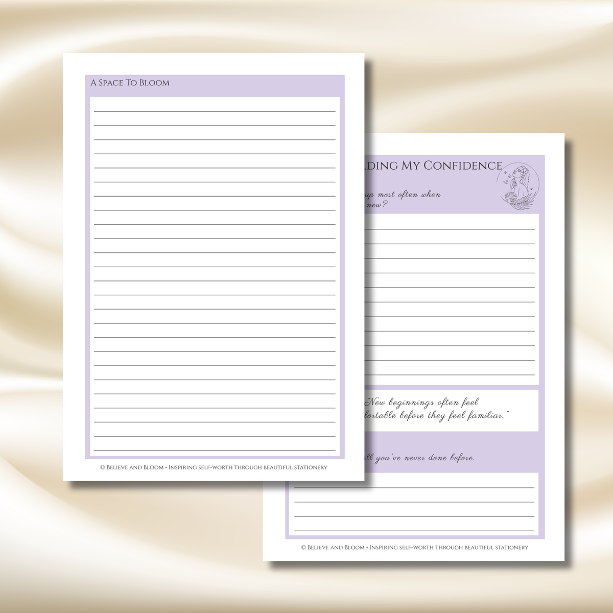 Two white writing paper notepads with lavender headers and lined writing pages, displayed on a soft beige satin background. One pad shows the cover page titled 'A SPICE TO BLOOM' and the other shows an interior page with a quote under the heading 'BUILDING MY CONFIDENCE'.